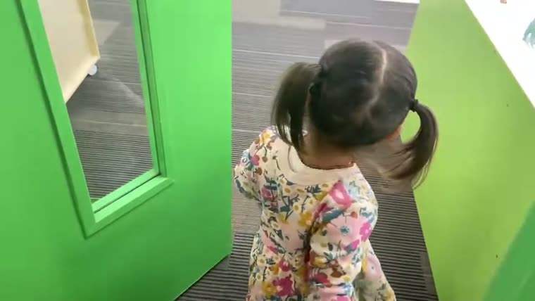 A child looking into a mirror set into a green wall