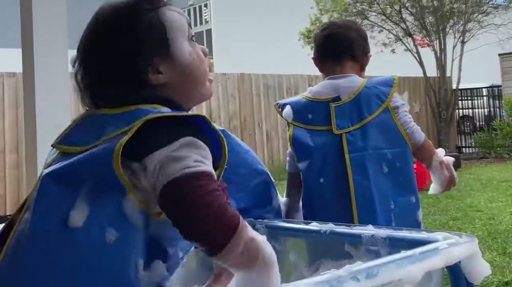 Two toddlers in smocks playing at a water tray outside